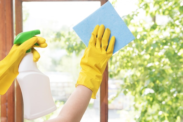 Niña ama de casa lava las ventanas de la casa con guantes de goma amarillos y con un trapo azul