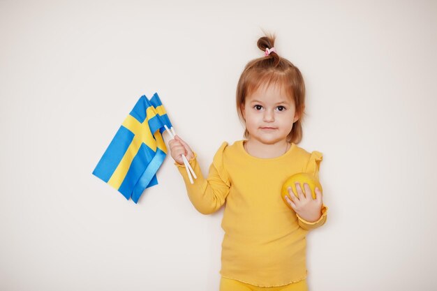 Niña en amarillo con limón y bandera de Suecia, fondo aislado.