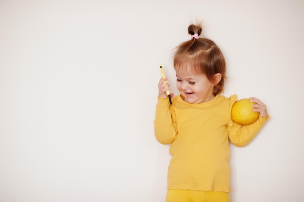 Niña en amarillo con limón y teléfono móvil, fondo aislado.