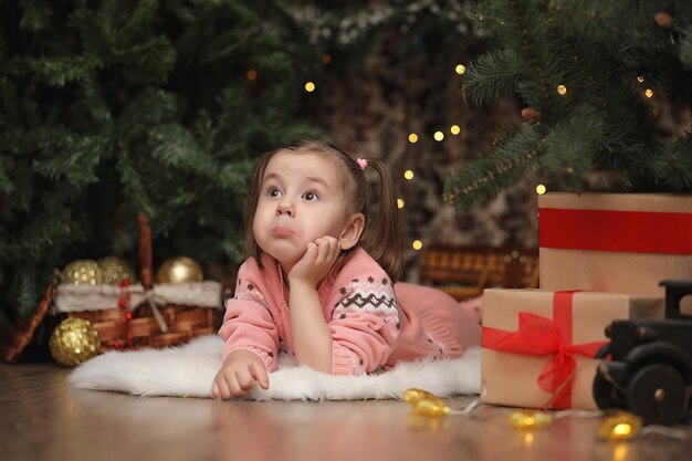 Niña en el ambiente navideño de año nuevo La niña está feliz con la Navidad y los regalos Un niño en el árbol de Año Nuevo con regalos