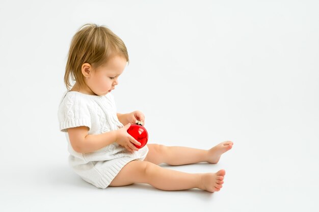 Una niña de un año está jugando con una bola roja de cristal de Navidad