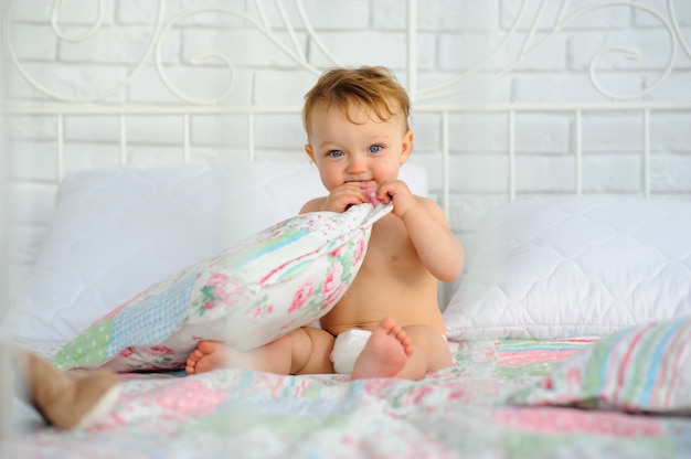 Niña de un año está sentado en la cama.