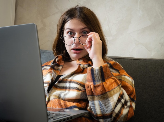 Niña con anteojos trabajando en una laptop sentada en casa en la cama.