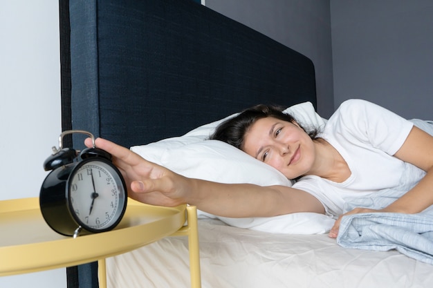 Foto la niña apaga el molesto despertador para seguir durmiendo. duerme un poco más