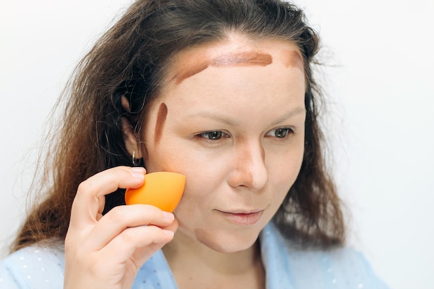 La niña aplica un corrector oscuro bronceador en la cara con una esponja.