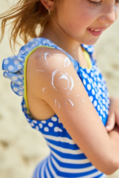 Niña con aplicar protector solar en el hombro en forma de sol de pie en la playa