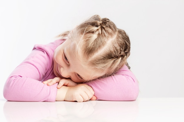 La niña apoyó la cabeza sobre la mesa. Pared blanca. De cerca.