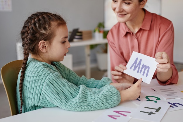 Niña aprendiendo el alfabeto inglés junto con el tutor en la mesa