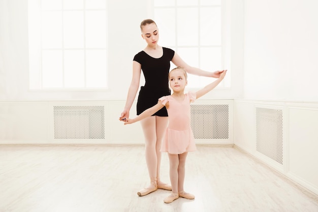 Niña aprendiendo ballet con espacio de copia de profesor. Linda pequeña bailarina entrenando ejercicios de danza clásica con entrenadora.