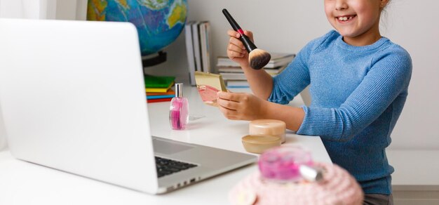niña aprendiendo maquillaje en polvo, brocha, rubor en computadora portátil en línea, aprendizaje a distancia