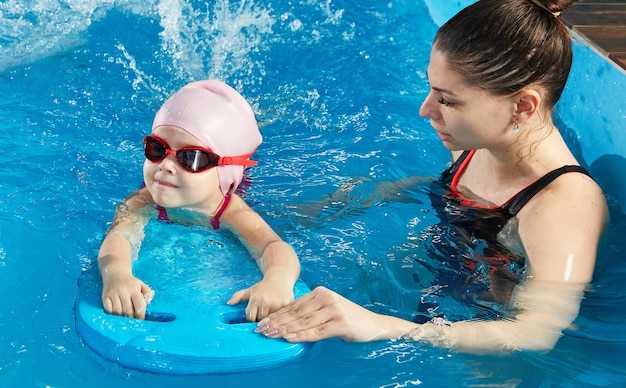 Niña aprendiendo a nadar en la piscina cubierta con tabla de billar y entrenador