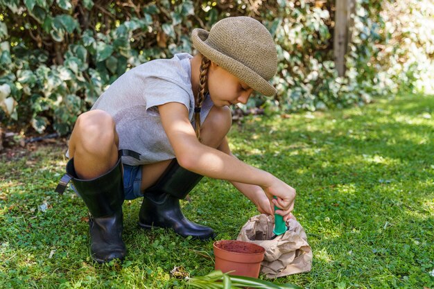 Foto niña aprendiendo el proceso para trasplantar una planta en una maceta nueva en el patio trasero