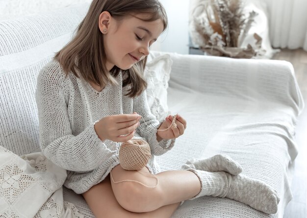 Niña aprendiendo a tejer, ocio en casa y concepto de costura.