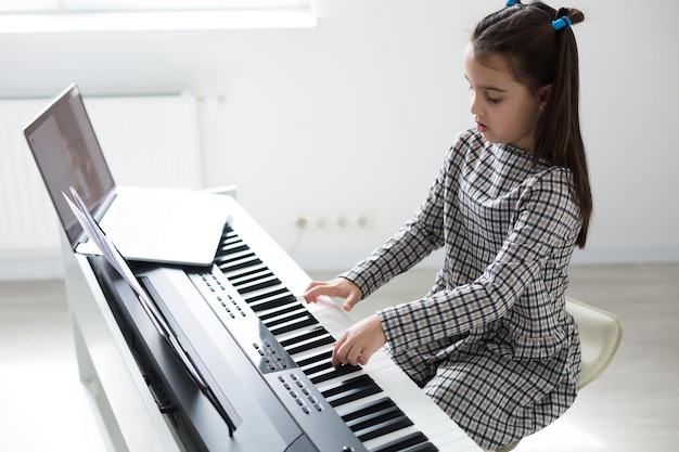 Niña aprendiendo a tocar el piano a distancia en línea durante la cuarentena. Concepto de coronavirus.