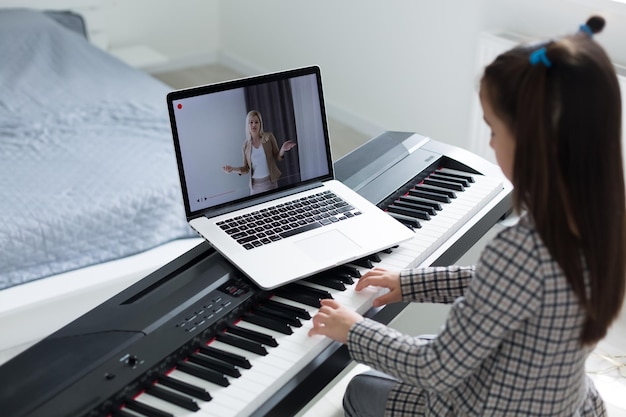 Niña aprendiendo a tocar el piano a distancia en línea durante la cuarentena. Concepto de coronavirus.