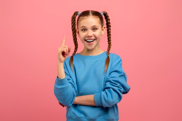 Niña apuntando hacia arriba con una sonrisa en fondo rosa