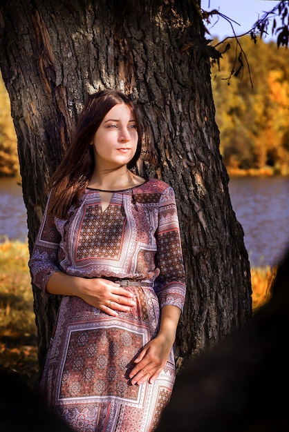 La niña se para en un árbol en el follaje de otoño.