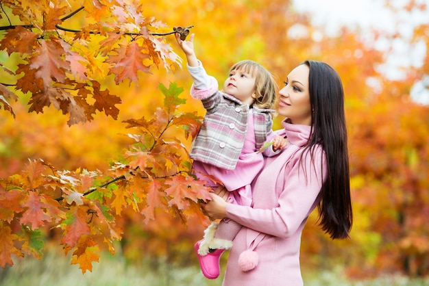 Una niña arranca las bellotas del árbol. Mamá e hija están jugando en el parque de otoño.