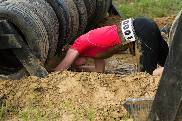 Foto la niña se arrastra por el barro, superando emocionalmente el obstáculo hecho de neumáticos.