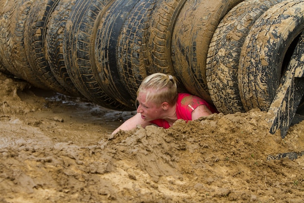 Foto la niña se arrastra por el barro, superando emocionalmente el obstáculo hecho de neumáticos.