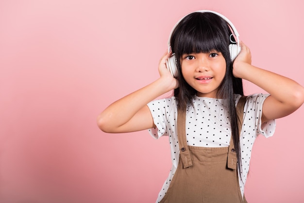 Niña asiática de 10 años sonriendo escuchando música con auriculares inalámbricos en la cabeza