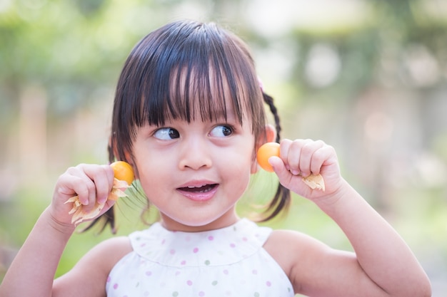 Foto la niña asiática adorable está actuando y sonríe con las frutas de la grosella espinosa de cabo