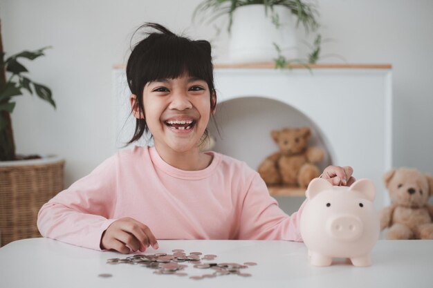 Niña asiática ahorrando dinero en una alcancía, aprendiendo a ahorrar, Kid ahorra dinero para la educación futura. Concepto de dinero, finanzas, seguros y personas