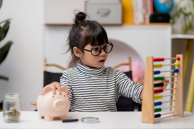 Niña asiática ahorrando dinero en una alcancía aprendiendo a ahorrar Niño ahorra dinero para la educación futura El dinero financia el seguro y el concepto de personas