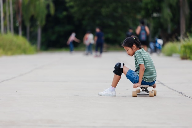 Niña asiática aprendiendo a andar en patineta al aire libre. Niño divirtiéndose y jugando patineta en la carretera durante el día. Actividad infantil y concepto de deporte extremo.