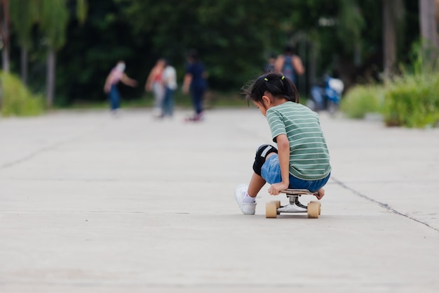 Niña asiática aprendiendo a andar en patineta al aire libre. Niño divirtiéndose y jugando patineta en la carretera durante el día. Actividad infantil y concepto de deporte extremo.