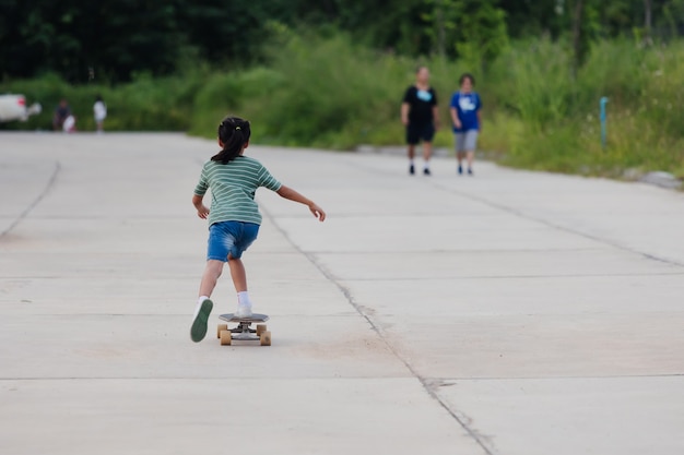 Niña asiática aprendiendo a andar en patineta al aire libre. Niño divirtiéndose y jugando patineta en la carretera durante el día. Actividad infantil y concepto de deporte extremo.