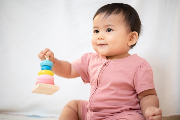 Una niña asiática de aproximadamente 1 año Jugando con un juguete de madera en la sala de estar de la casa Un lindo bebé con un vestido rosa Quédate con los padres en la casa