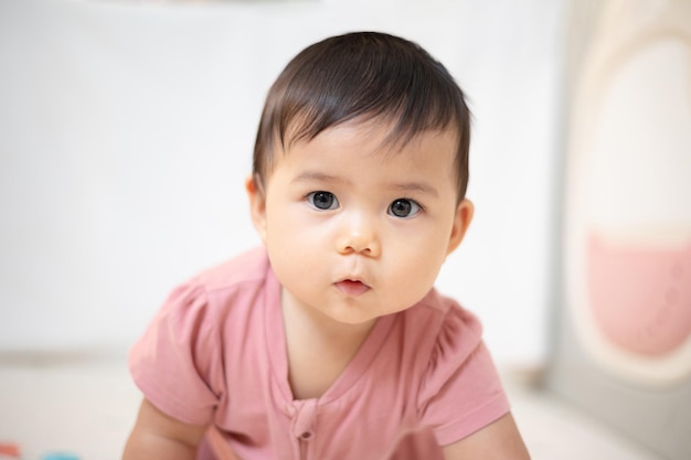 Una niña asiática de aproximadamente 1 año jugando en la sala de estar de la casa Un lindo bebé con un vestido rosa Quédate con los padres en la casa