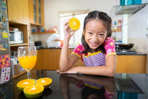 Niña asiática bebiendo jugo de naranja en la cocina