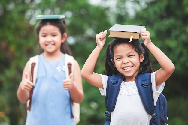 niña asiática con bolsa de la escuela y su hermana puso un libro en la cabeza juntos