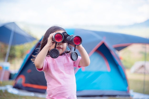 Niña asiática busca en binoculares en el campamento