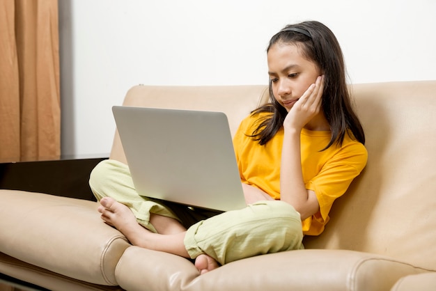 La niña asiática con una computadora portátil se siente cansada en la clase de la escuela en línea en casa. Educación en línea durante la cuarentena