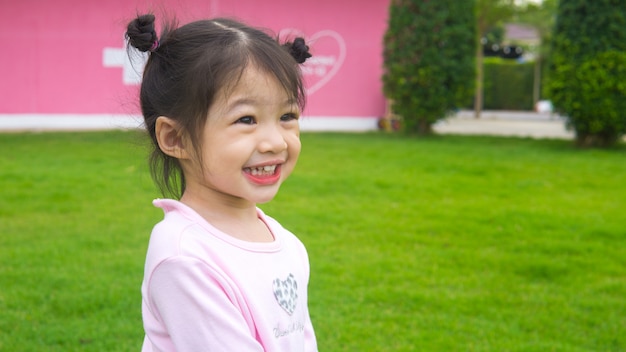 Niña asiática corriendo y caminando en campo de hierba.