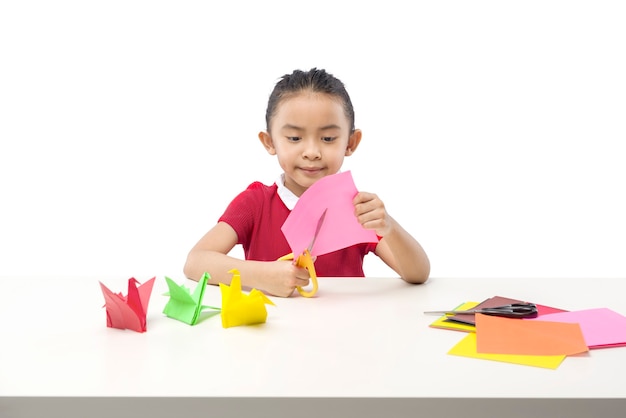 Niña asiática cortando un papel aislado sobre fondo blanco.