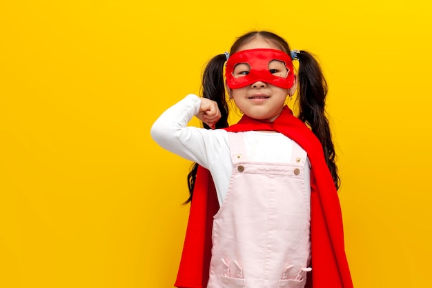 Niña asiática con disfraz de Superman y máscara mostrando bíceps y gesto de poder niño coreano