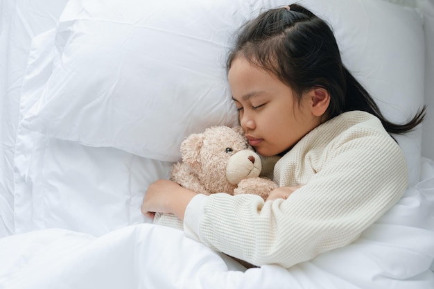 Niña asiática durmiendo y abrazando oso de peluche en el dormitorio