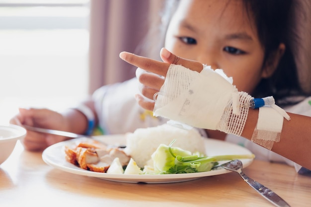 Niña asiática enferma que come alimentos saludables para el almuerzo sola mientras permanece en habitaciones privadas de pacientes en el hospital. Concepto de salud y estilo de vida.