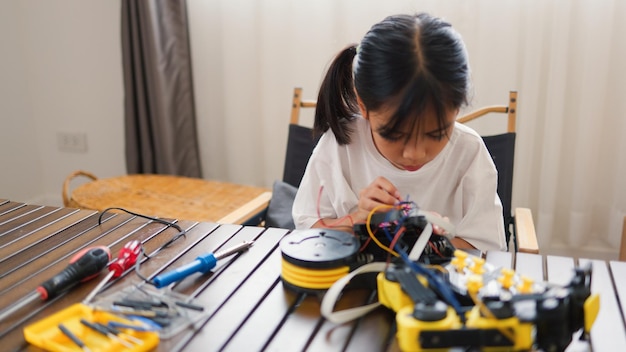 Niña asiática ensamblando piezas de robots en casa aprendiendo STEM y electrónica Desarrollando habilidades de ingeniería pensamiento lógico y resolución de problemas a través de la educación de codificación manual para niños