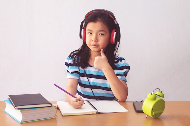 Niña asiática escribiendo un libro y auriculares escuchando música.