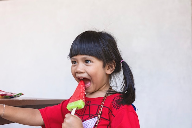 Una niña asiática está comiendo felizmente helado.