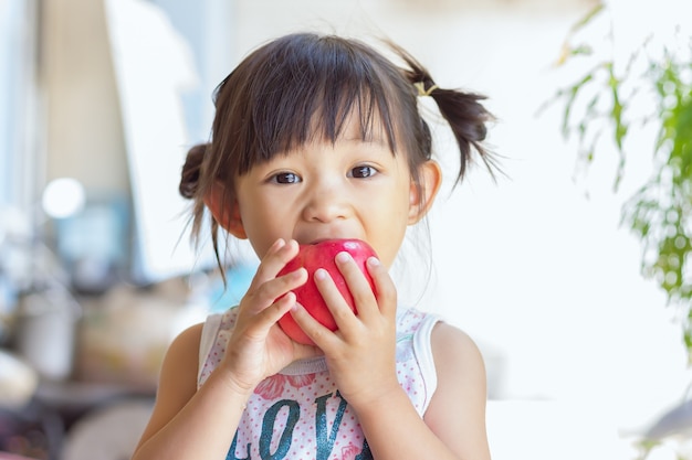 Niña asiática feliz comiendo y mordiendo una manzana roja.