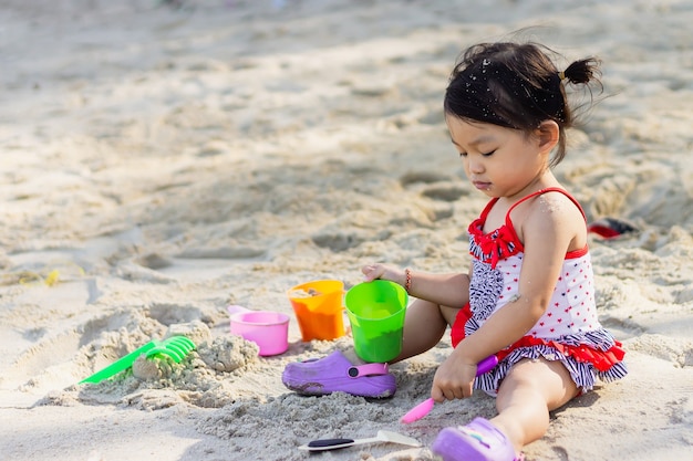 Niña asiática feliz jugando arena en la playa en el mar. En la temporada de verano.