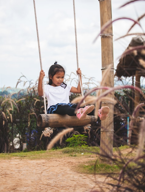 Niña asiática feliz niño divirtiéndose para jugar en columpios de madera en el patio de recreo