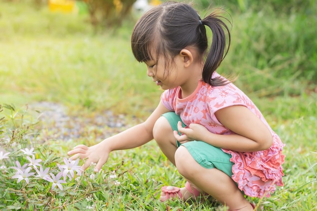 Foto niña asiática feliz recogiendo y tocando las flores y la hierba en el campo del jardín