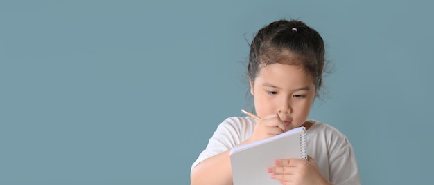 Una niña asiática feliz shandwrite en el aprendizaje del cuaderno usando lecciones de Internet en cuarentena